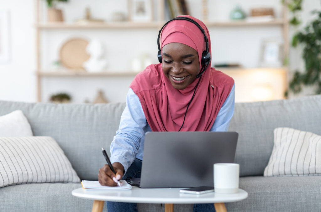 Black muslim lady studying online with laptop and headset