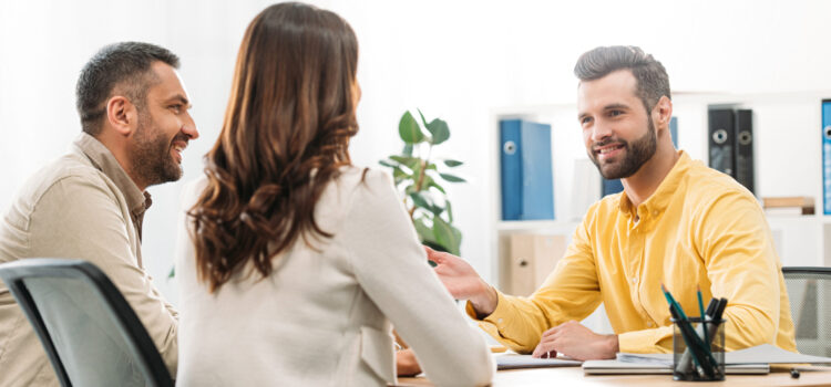 advisor sitting at table and smiling to man and woman in office