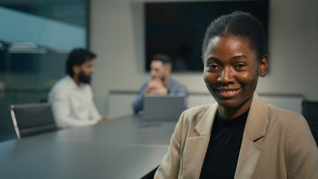African American ethnic professional businesswoman hr manager employer woman company CEO expert female leader looking at camera sitting at table on background of colleagues business meeting in office