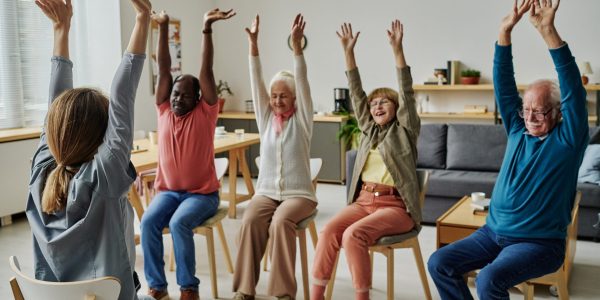 Group of senior people sitting on chairs and exercising during sport training with instructor