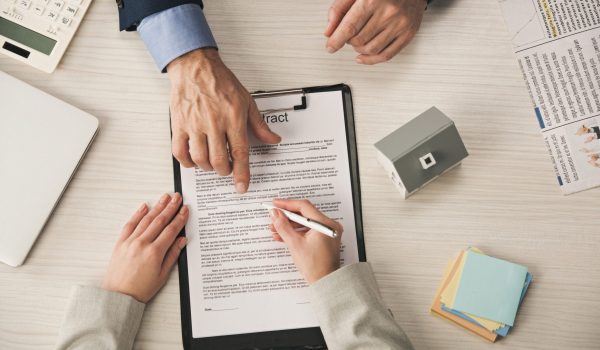 top view of agent pointing with finger at clipboard with contract lettering near woman