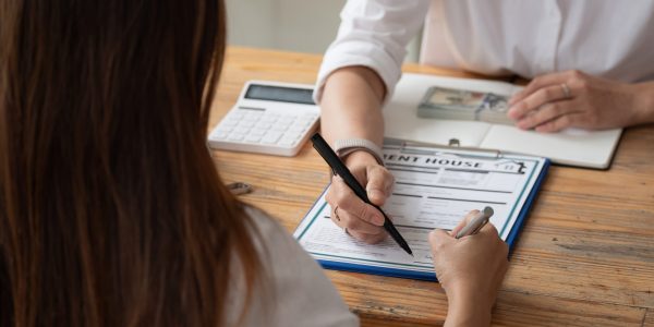 close up view hands of businessman signing leasing home documents and have a apartment keys on paperwork.