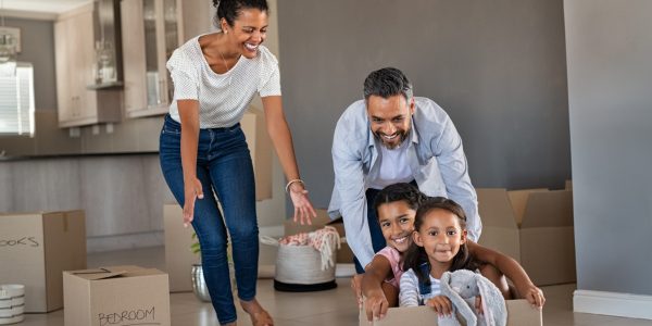 Happy indian father playing with daughters sitting in carton box at new home. Happy multiethnic family having fun together in new house. Smiling dad pushing excited little girls in cardboard box after relocation.