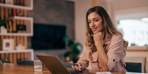 Young woman, browsing for jobs, at home, on her laptop, while writing.