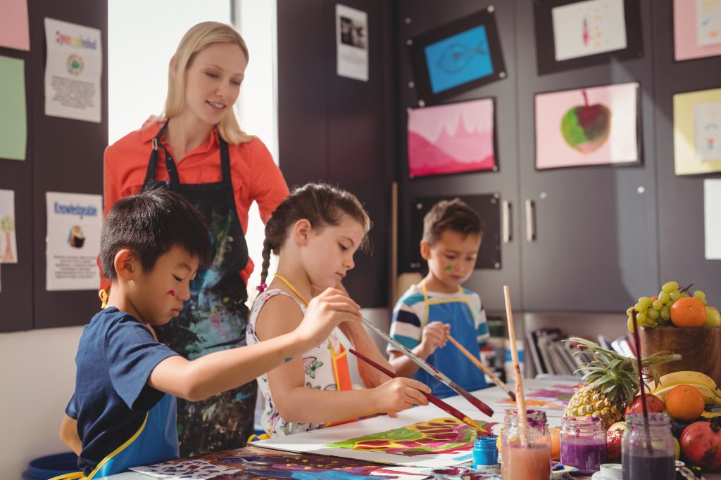 Teacher assisting schoolkids in drawing class at school